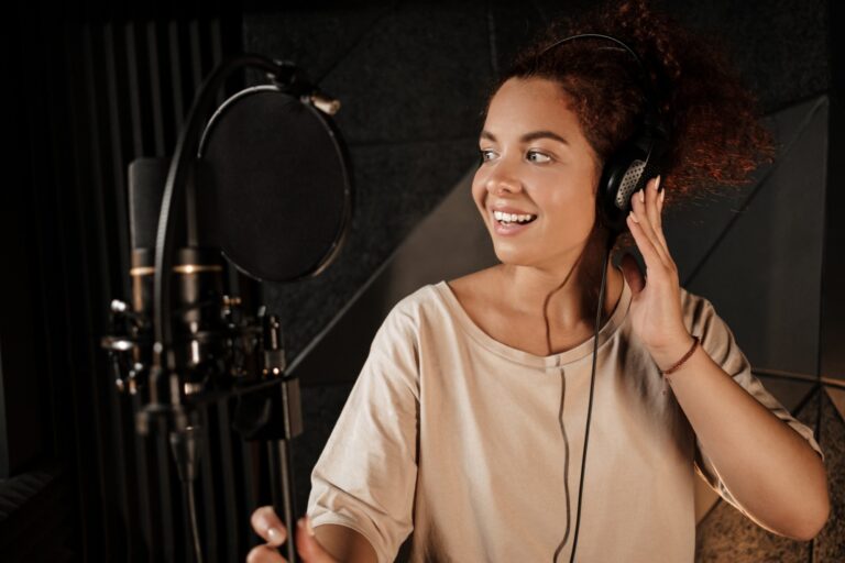 Cantora com fones de ouvido sorrindo em frente ao microfone em um estúdio de gravação