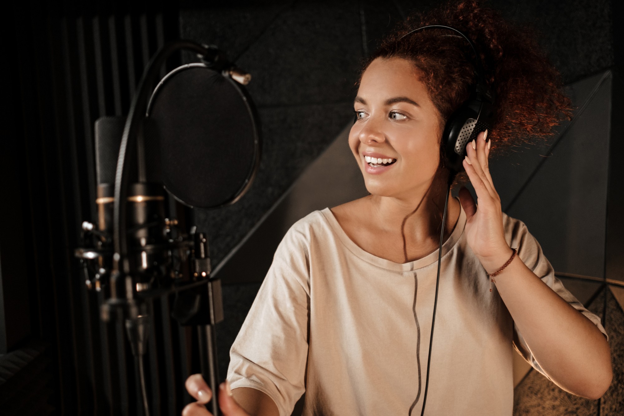 Cantora com fones de ouvido sorrindo em frente ao microfone em um estúdio de gravação